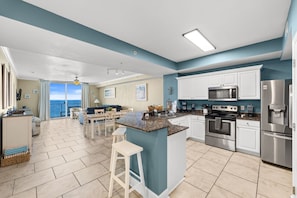 A modern kitchen with a central island, white cabinetry, stainless steel appliances, and a view to the outside. - Beachfront 20th Floor • Ocean View 2BR/2BA Condo • Sleeps up to 8 (Panama City Beach)