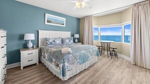 Una camera da letto con un letto, un comodino, una lampada e vista sull'oceano attraverso una finestra.