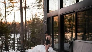 Un edificio moderno con grandes ventanales, un jacuzzi y una terraza de madera rodeada de nieve.