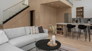 Una sala de estar moderna con un sofá gris, una mesa de centro negra y un comedor con una cocina al fondo.