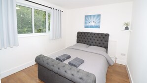 Un dormitorio con una cama grande, un banco tapizado en gris y una ventana con cortinas.