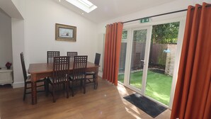 Un comedor con una mesa y sillas de madera, un cuadro en la pared y un ventanal corredizo que da a un jardín.