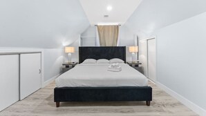 A modern bedroom with a large bed, bedside tables with lamps, and a wardrobe. - Modern 5BR Duplex w/ Easy NYC Access & Parking (Bayonne)