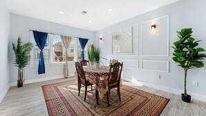 A dining area with a table set for four, surrounded by chairs, in a room with white walls and a patterned rug. - Modern 5BR Duplex w/ Easy NYC Access & Parking (Bayonne)