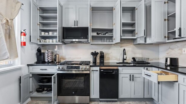 A modern kitchen with grey cabinets, stainless steel appliances, and a marble backsplash. - Modern 5BR Duplex w/ Easy NYC Access & Parking (Bayonne)