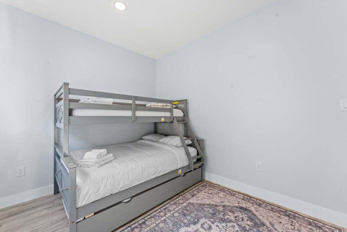A bunk bed in a room with light gray walls and a patterned rug on the floor.