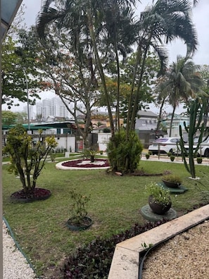 A landscaped garden with palm trees, a circular flower bed, and a variety of potted plants. - Apto com Piscina e Sauna Perto da Praia da Barra (Rio de Janeiro)