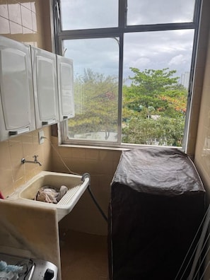 A small bathroom with a window, a sink, and cabinets. - Apto com Piscina e Sauna Perto da Praia da Barra (Rio de Janeiro)