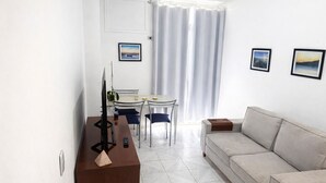 A modern living room with a sofa, a dining table with chairs, and two framed pictures on the wall. - Apto com Piscina e Sauna Perto da Praia da Barra (Rio de Janeiro)