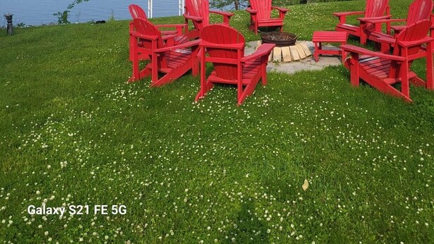 A lakeside setting with red Adirondack chairs arranged around a fire pit, overlooking a calm lake and distant hills. - Lakebreeze Retreat (tweed)