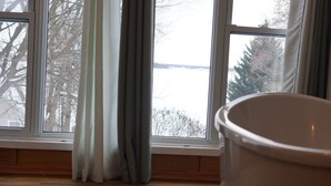 A room with a large window, wooden flooring, and a white bathtub. - Lakebreeze Retreat (tweed)