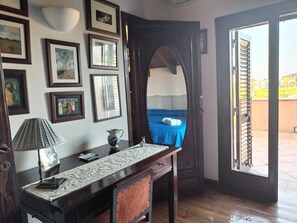 A room with a bed, a desk with a lamp, a vase, and framed pictures on the wall.