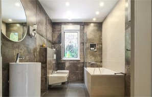 Une salle de bain moderne avec un grand miroir, deux lavabos, des toilettes et une baignoire.