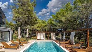 A rectangular swimming pool with wooden loungers and umbrellas on a deck, surrounded by trees and a clear sky. - Awesome home in Pula with private swimming pool, can be inside or outside (Pula)