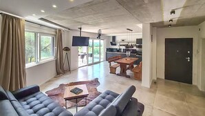A modern living room with a leather sofa, a coffee table, and a dining area with a wooden table and benches. There is a kitchen in the background with a dark door. - Awesome home in Pula with private swimming pool, can be inside or outside (Pula)