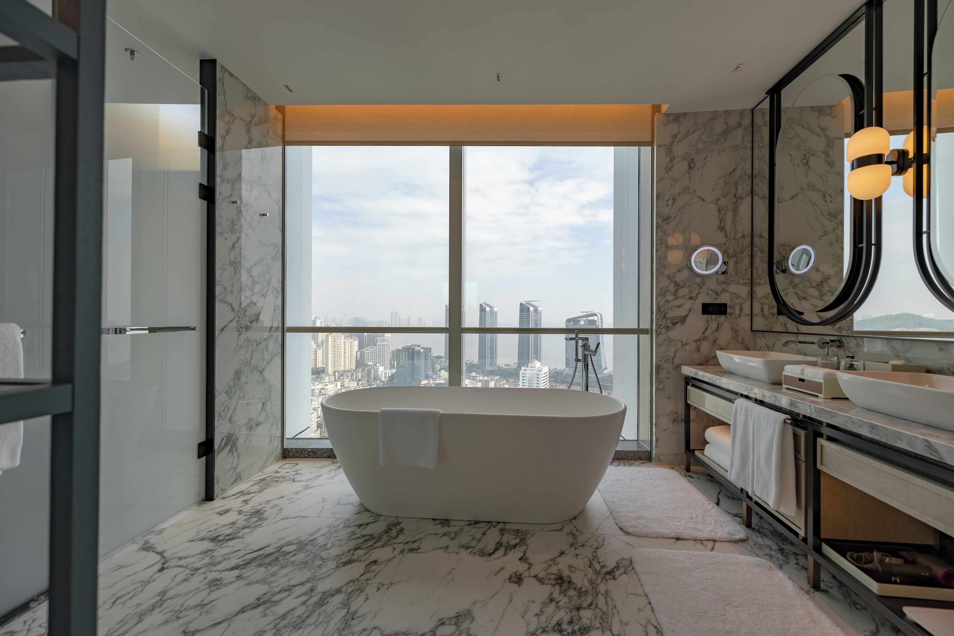 Ein modernes Badezimmer mit freistehender Badewanne, großen Fenstern und Blick auf die Stadt.