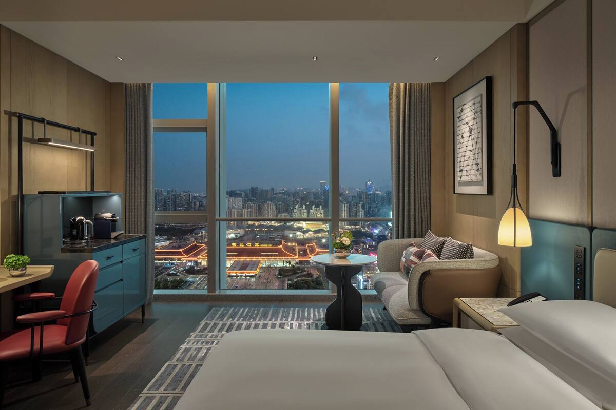 Una habitación de hotel con vistas a la ciudad, un escritorio con hervidor, un sofá y una cama.