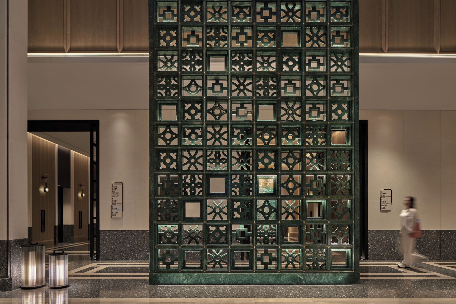 A modern interior with a decorative metal partition, a polished marble floor, and a corridor leading to a restroom.