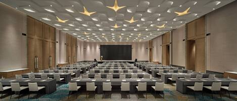 A conference room with rows of tables and chairs, a large screen, and a patterned ceiling.