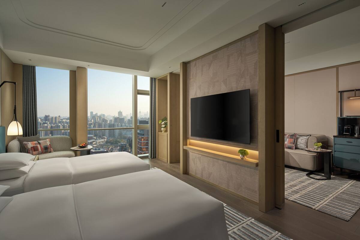 Habitación de hotel moderna con una cama grande, televisión, sofá y vista a la ciudad.