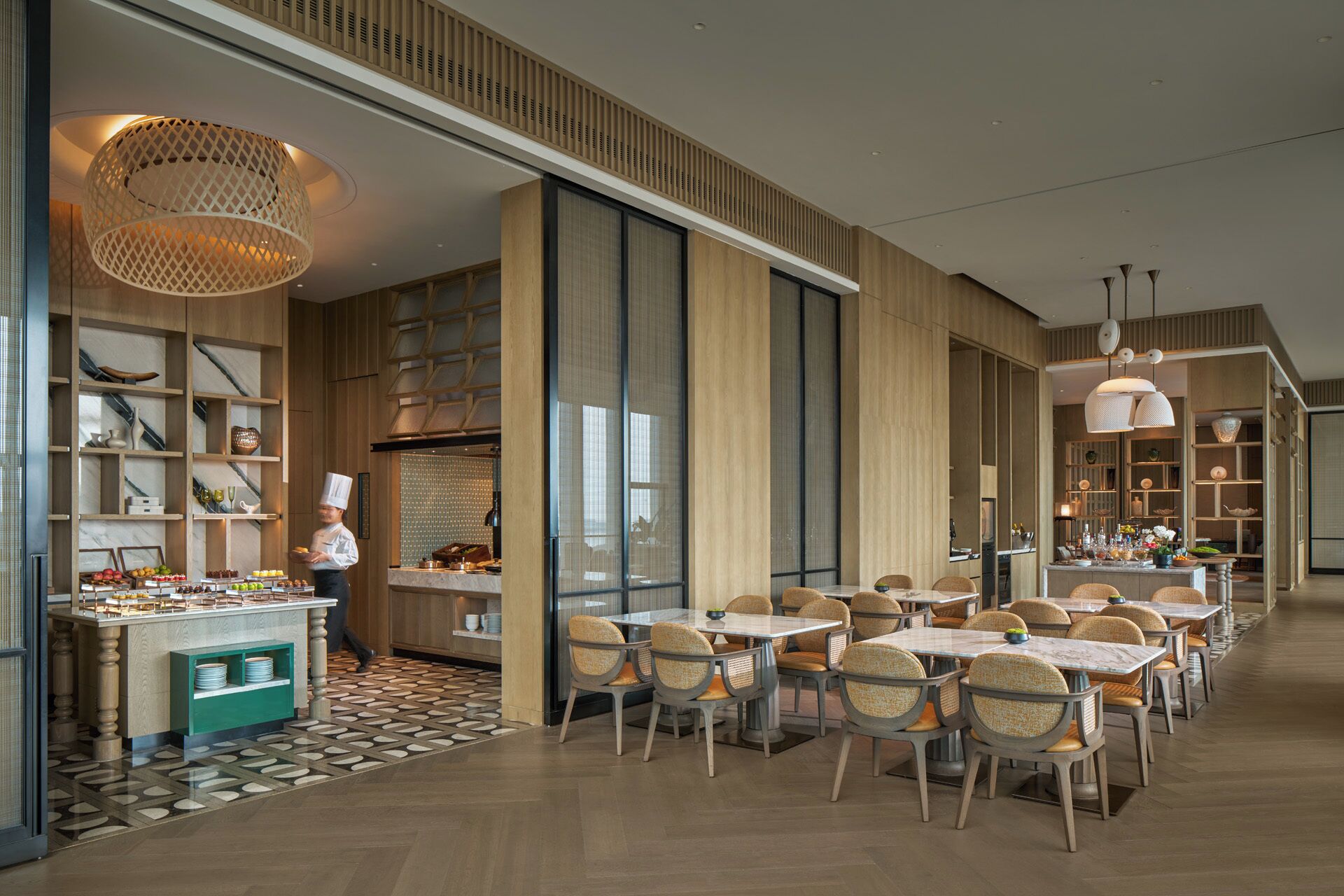 A modern restaurant with a chef preparing food, wooden paneling, and a variety of seating arrangements.