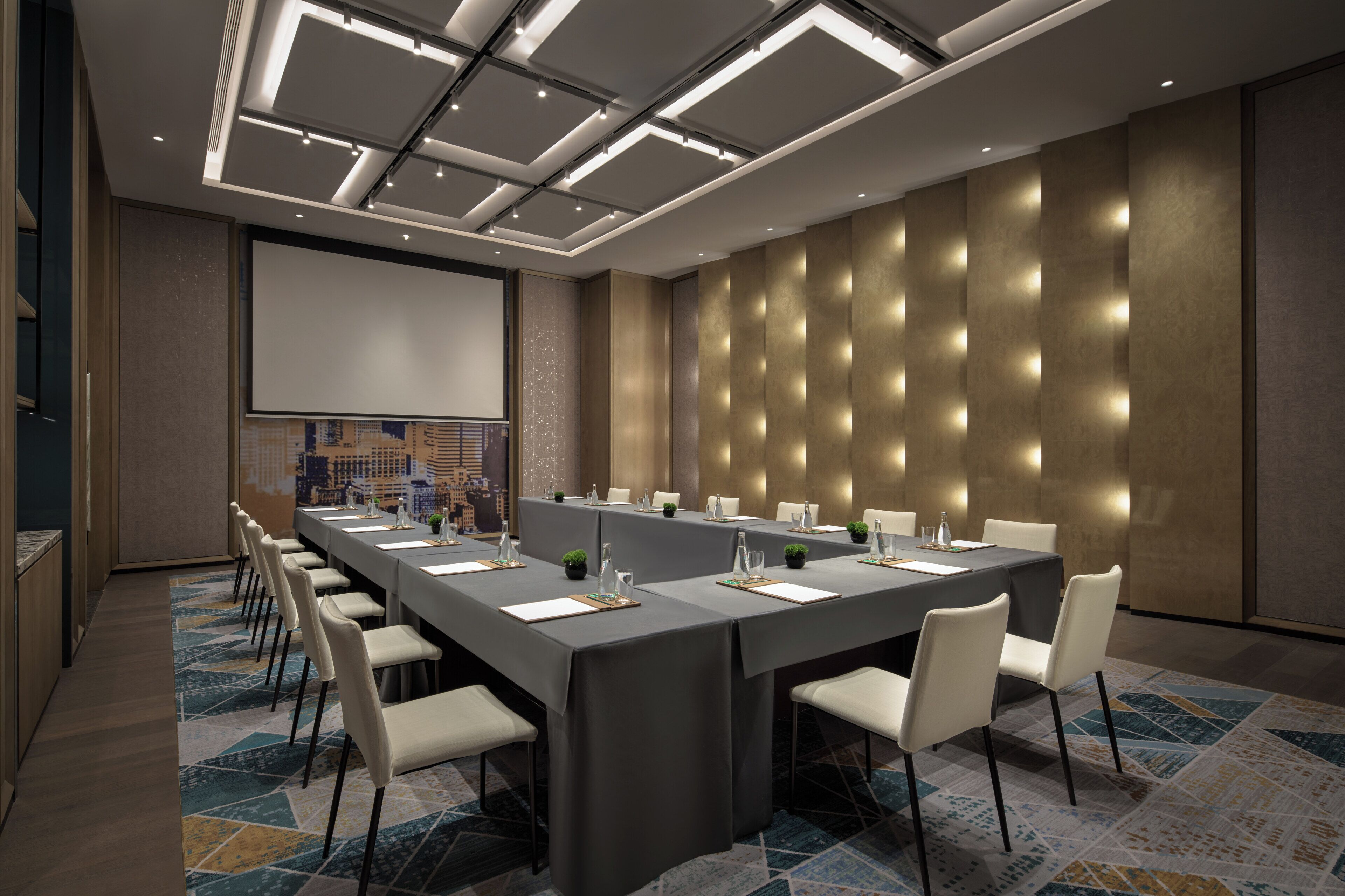 A conference room with a long table, chairs, a projector screen, and a cityscape view.