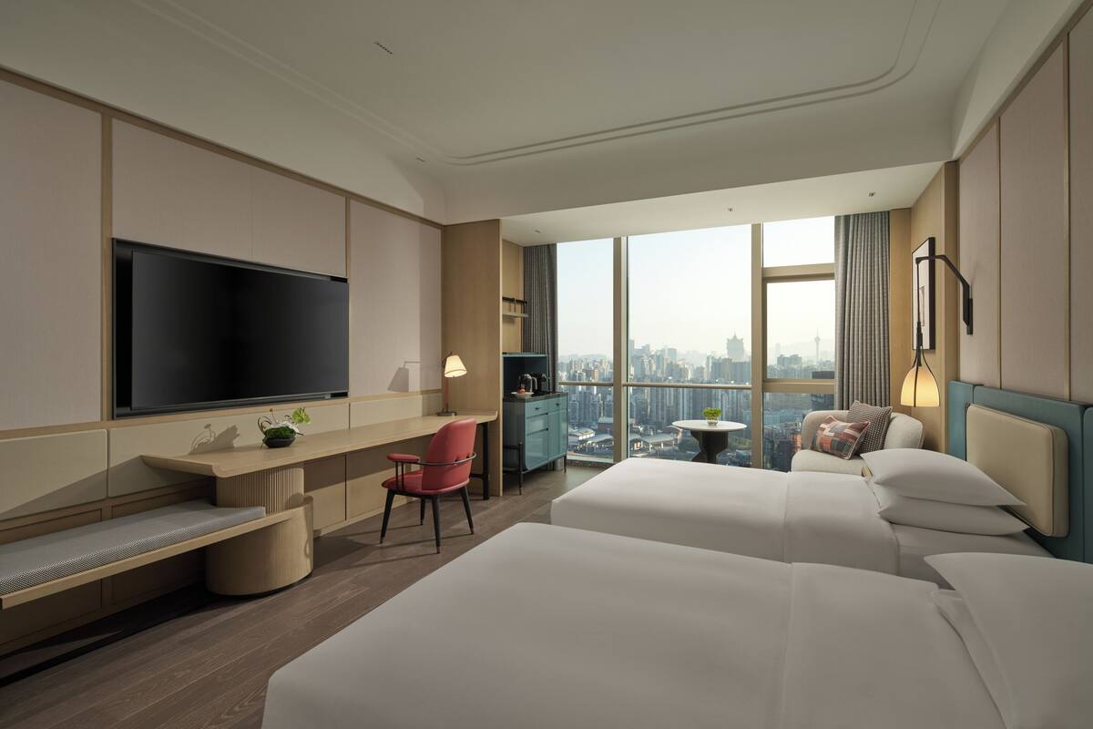 Habitación de hotel con una televisión grande, un escritorio, una silla, una cama y vistas a la ciudad.
