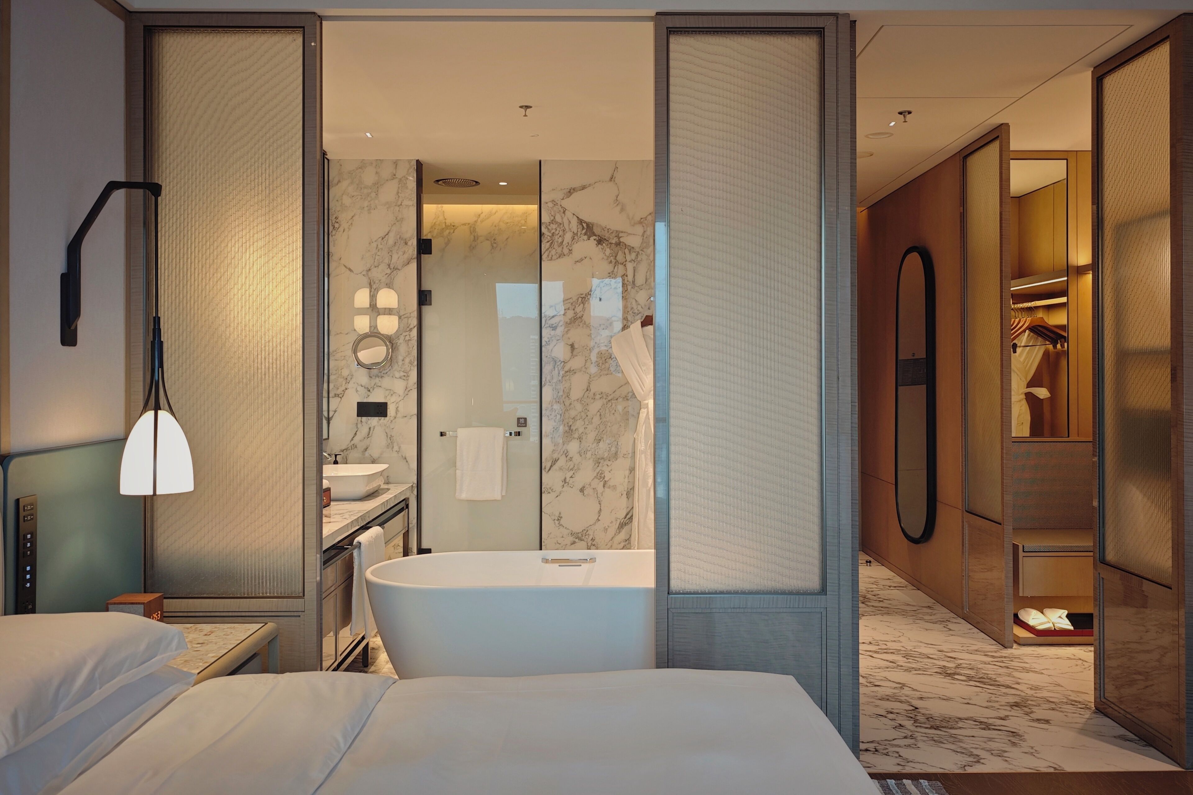 A modern hotel room with a large bed, a separate bathroom with a bathtub, a vanity with a mirror, and a walk-in closet.