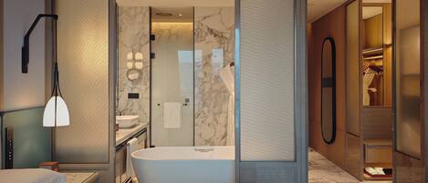 A modern hotel room with a large bed, a separate bathroom with a bathtub, a vanity with a mirror, and a walk-in closet.