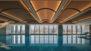 Una piscina interior moderna con vistas a la ciudad, amplios ventanales y un diseño de techo de madera.