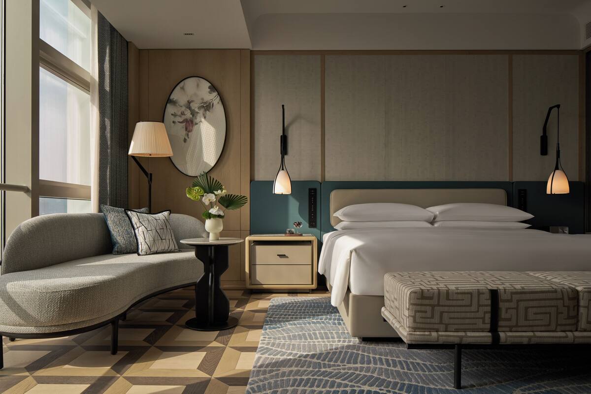Habitación de hotel con sofá, cama, mesita de noche, lámpara y una obra de arte en la pared.