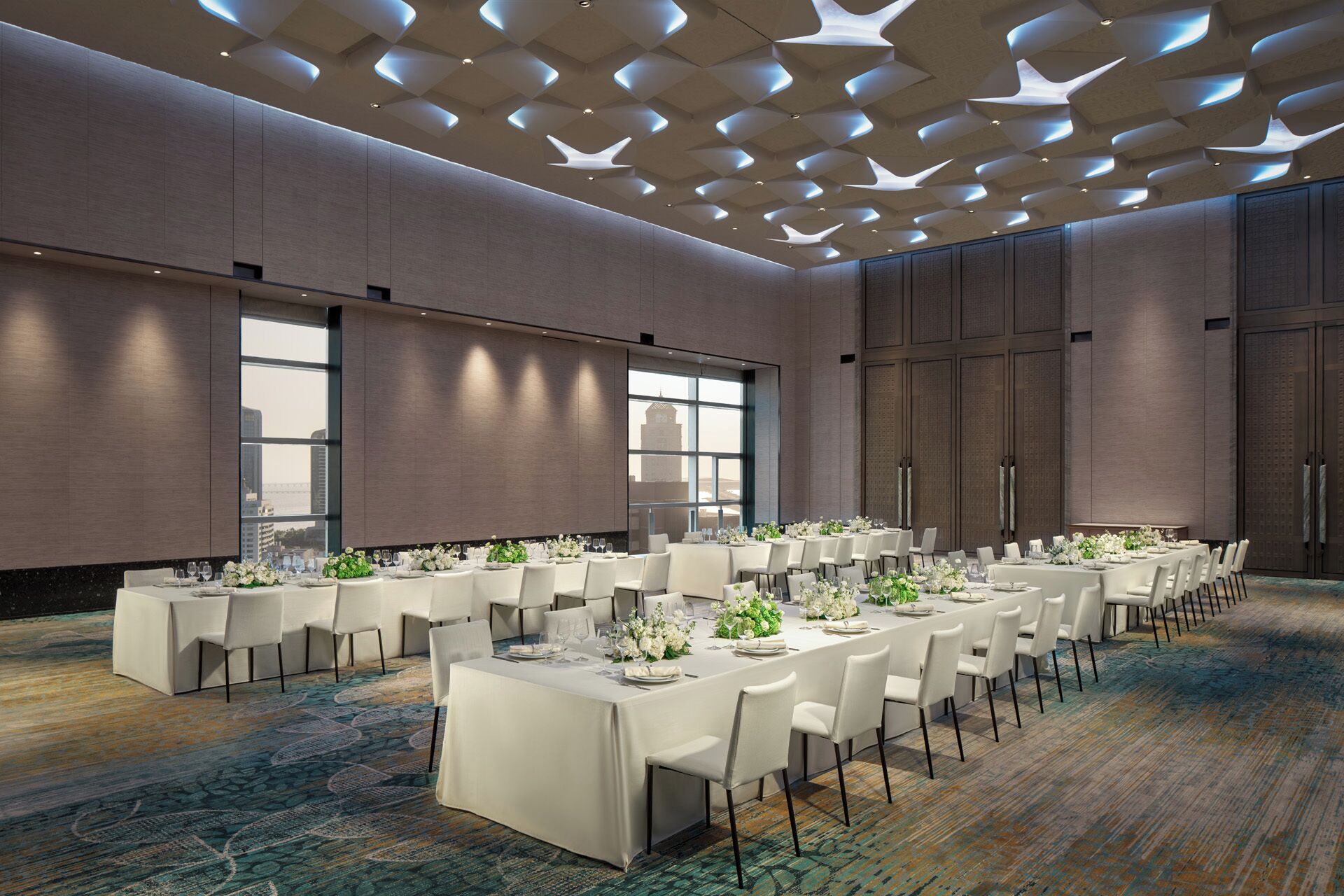 A conference room with a long table set for a meeting, large windows, and a patterned carpet.