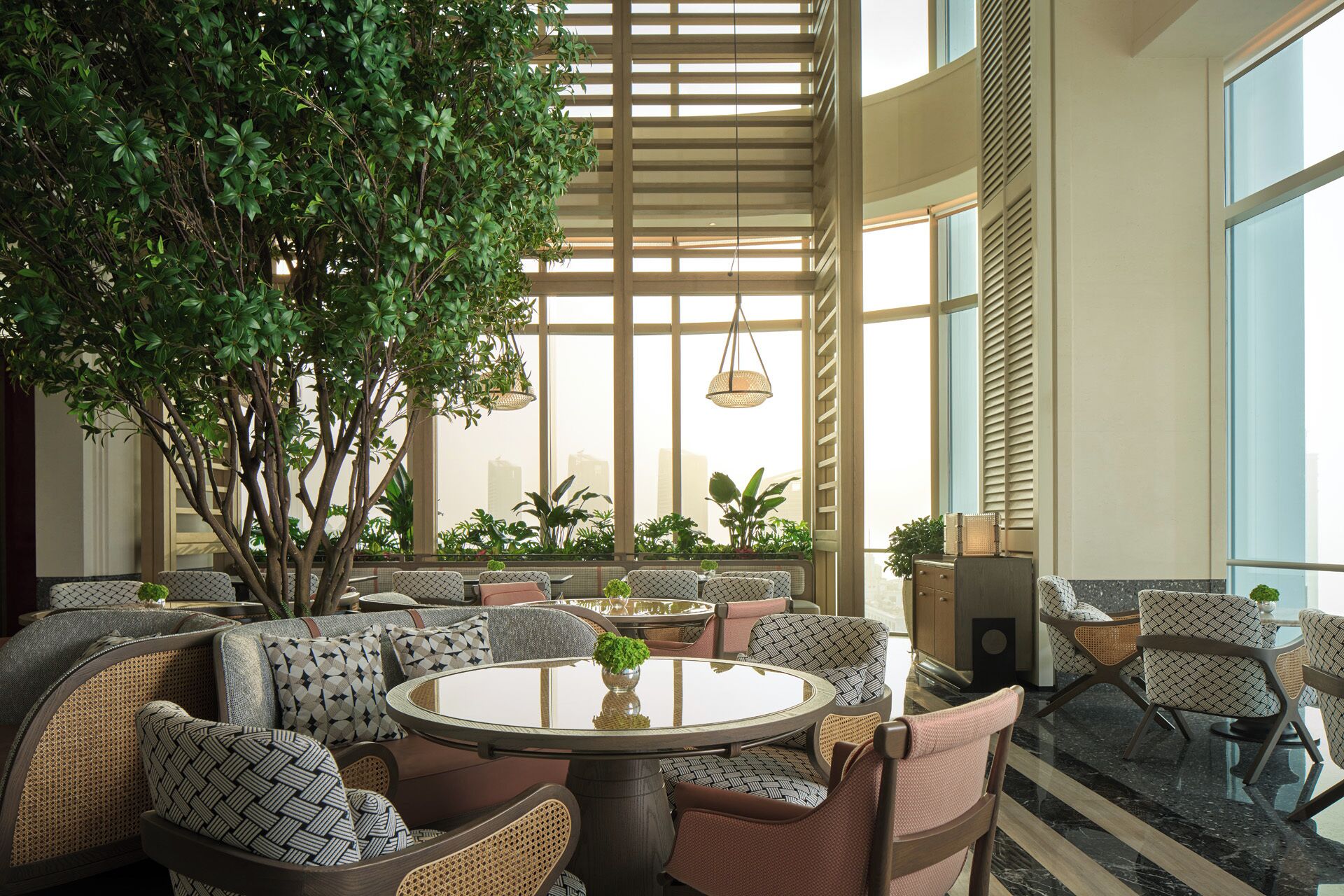 A spacious indoor seating area with a large tree, round tables, and patterned chairs.