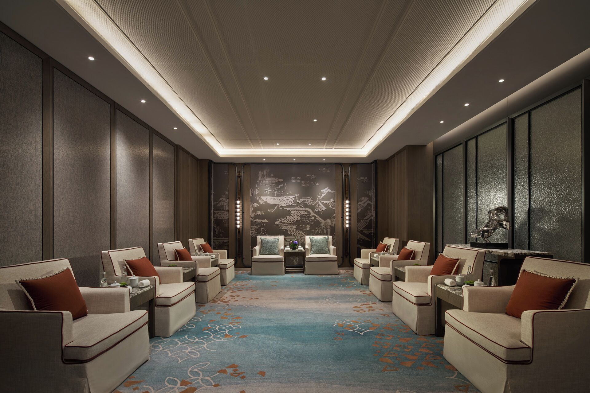 A hotel room with a large, patterned carpet, multiple seating areas, and a decorative wall mural.