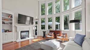 Ein geräumiges Wohnzimmer mit Kamin, einem großen darüber angebrachten Fernseher und einer gemütlichen Sitzecke mit Sofa und Sesseln.