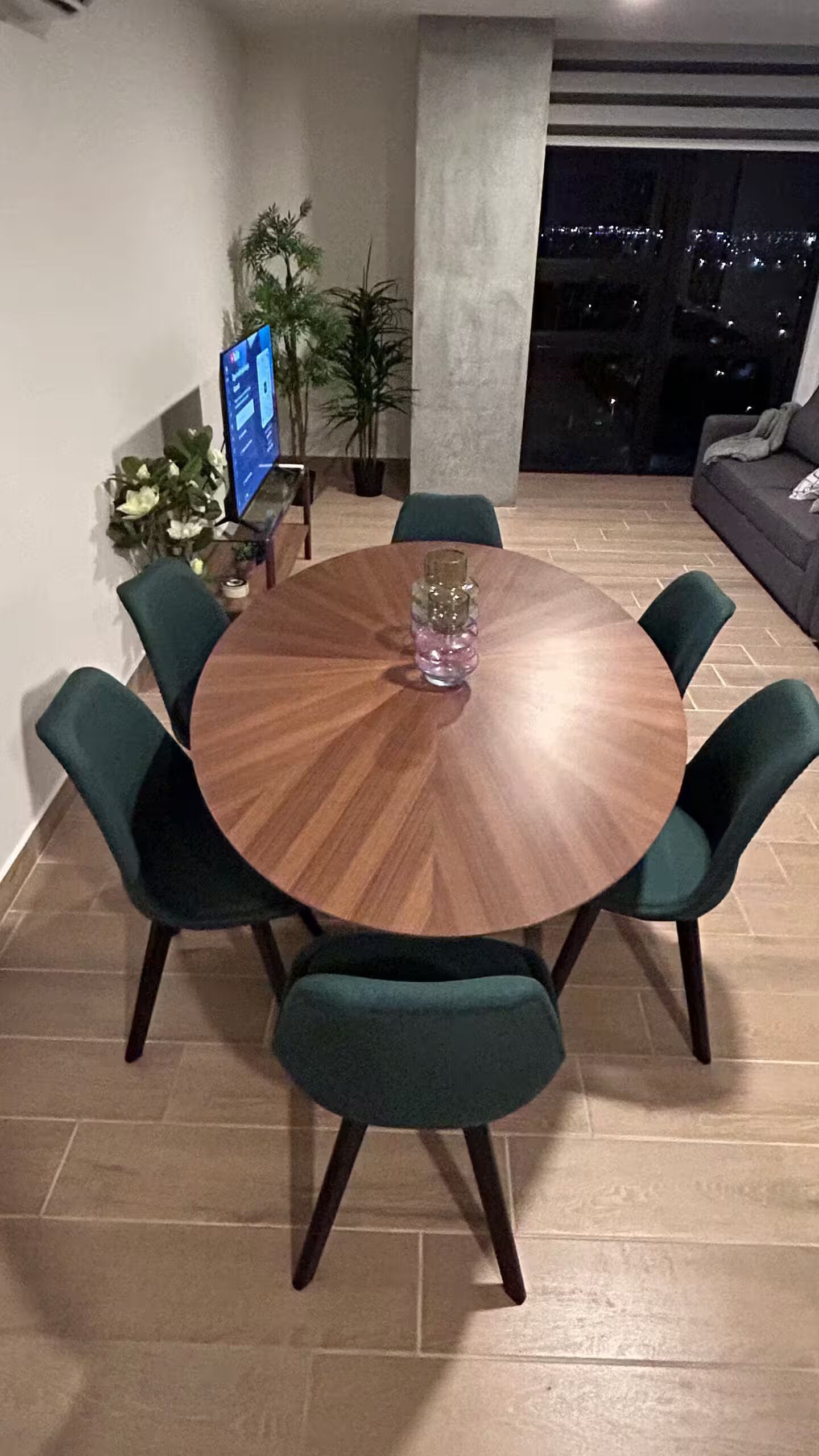 Ein runder Holztisch mit sechs Stühlen, einer Zimmerpflanze und einem Fernseher auf einem Schrank.