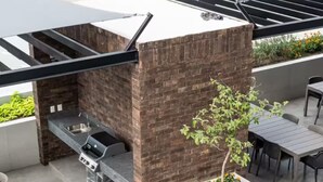 An outdoor patio with a brick barbecue area, a white planter with a small tree, and a seating area with tables and chairs. - Chic 3BR Prime Spot - 12 guests (Monterrey)