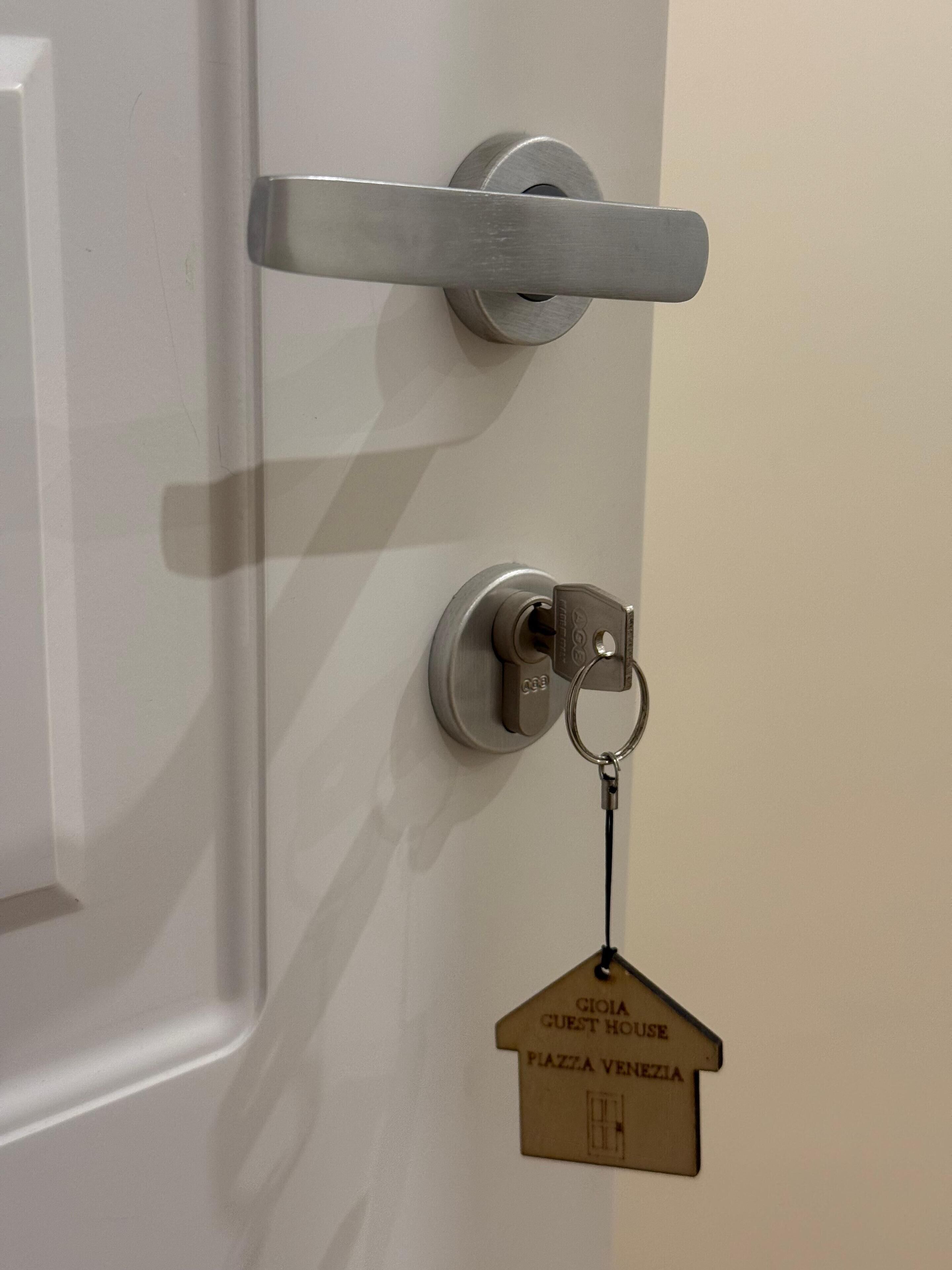 A door with a keyhole and a keychain with a house-shaped key tag labeled "GIOIA GUEST HOUSE PLAZA VENEZIA".