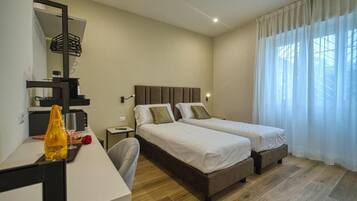 Een hotelkamer met twee bedden, een bureau met stoel, een spiegel en een raam met gordijnen.
