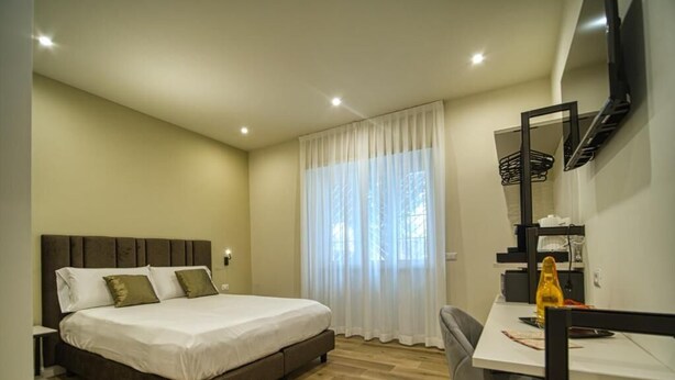 A bedroom with a bed, a desk, a chair, a television, and a window with curtains.
