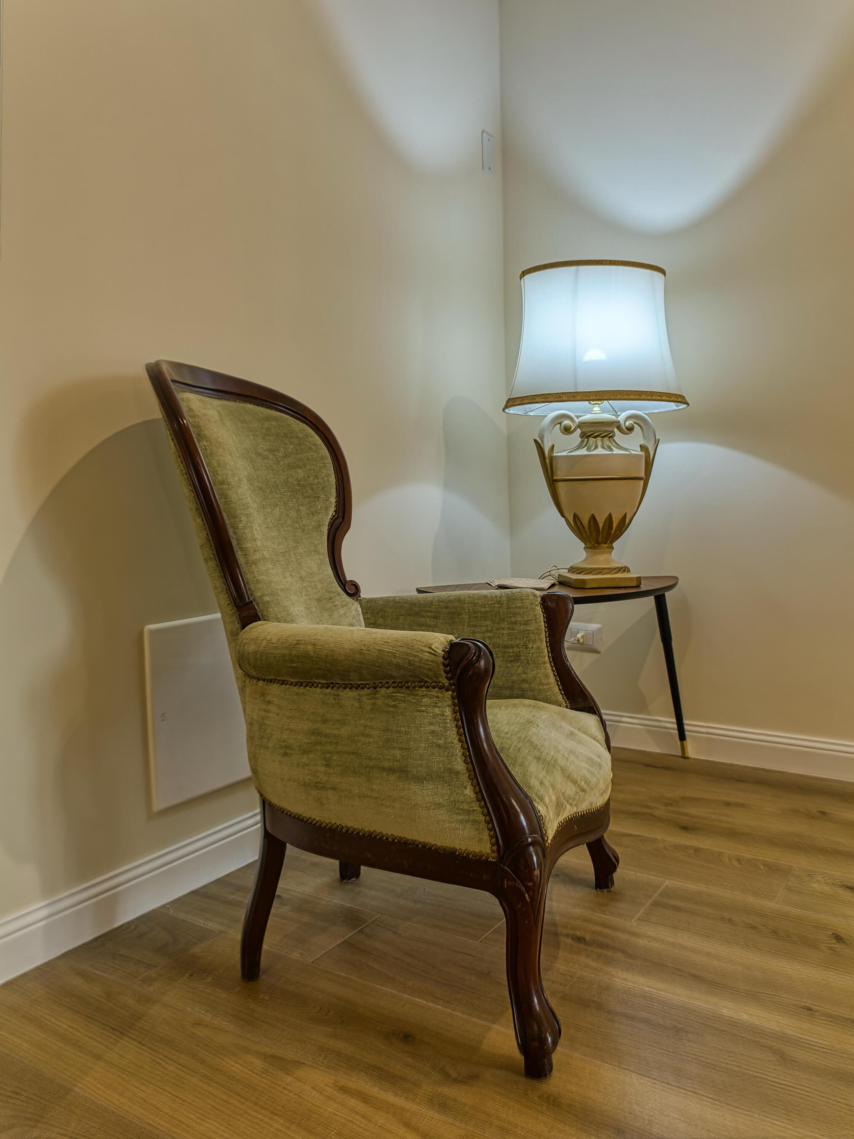 A wooden chair with a high backrest and armrests, positioned next to a small table with a lamp.