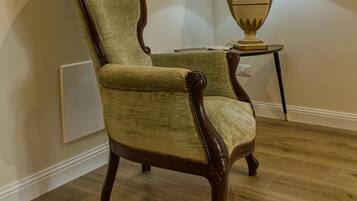 A wooden chair with a high backrest and armrests, positioned next to a small table with a lamp.
