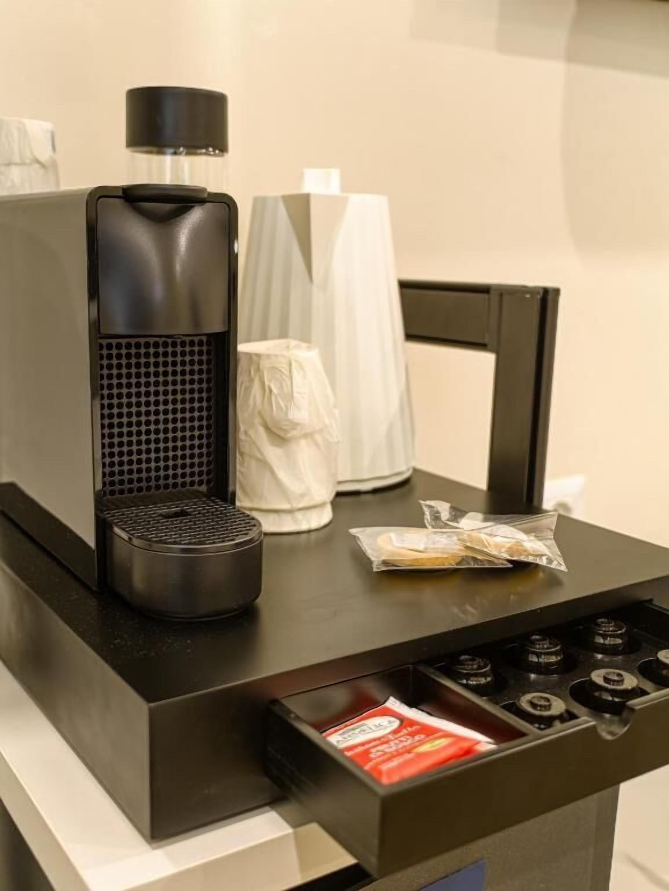 Uma máquina de café, uma caixa de lenços e um saco de petiscos sobre uma mesa.