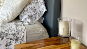 A neatly made bed with floral bedding, a grey headboard, and a wooden nightstand with a candle and a glass container. - Peaceful 2-bedroom, 2 bath  apartment in Boquete with vista to Baru (Boquete)