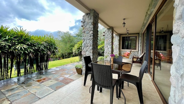 A covered patio with stone pillars, a glass table, and chairs. - Peaceful 2-bedroom, 2 bath  apartment in Boquete with vista to Baru (Boquete)