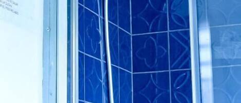 A shower with a handheld showerhead and a vertical rain showerhead, set against a blue tiled wall with a floral pattern.