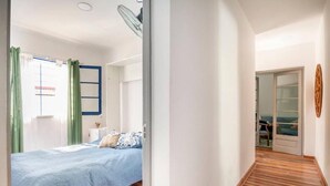 Une chambre à coucher avec un lit, une fenêtre avec des rideaux, un ventilateur et une vue sur un balcon.