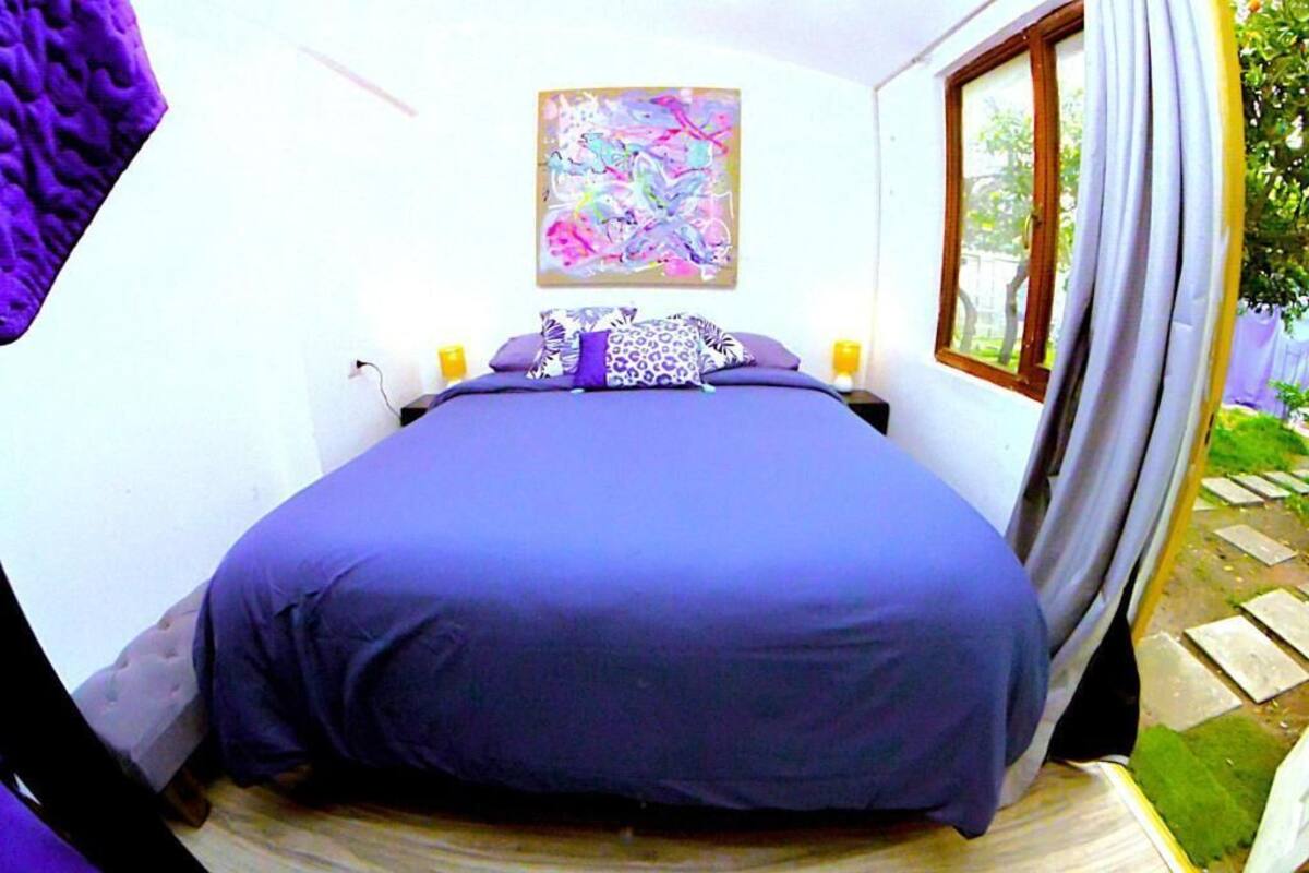 Une chambre avec un grand lit, un tableau abstrait aux couleurs vives accroché au mur et une fenêtre avec des rideaux.