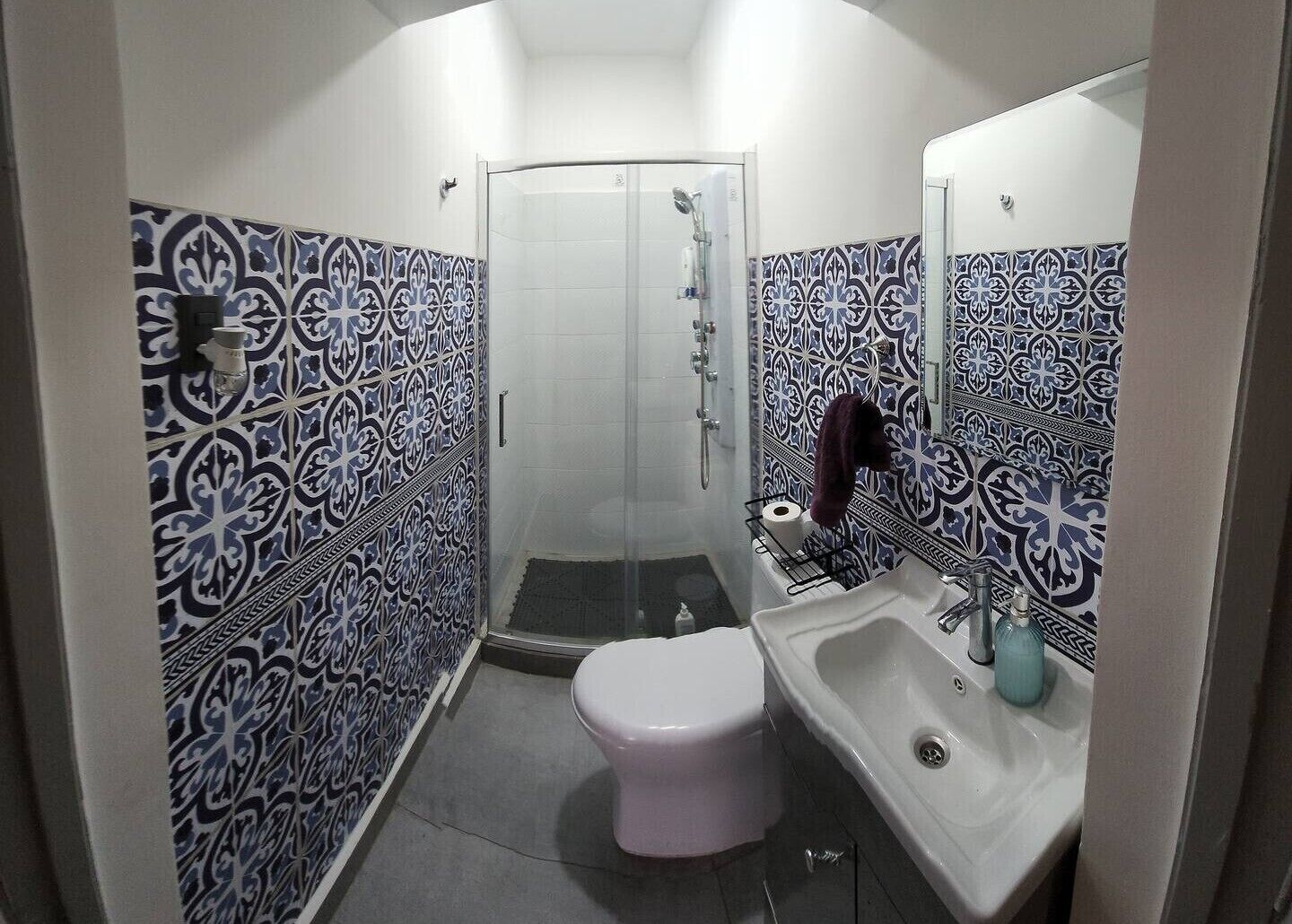 Un baño pequeño con inodoro, lavamanos y ducha. Las paredes están cubiertas de azulejos con un diseño azul y blanco.