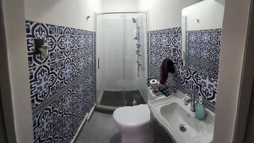 Un baño pequeño con inodoro, lavamanos y ducha. Las paredes están cubiertas de azulejos con un diseño azul y blanco.
